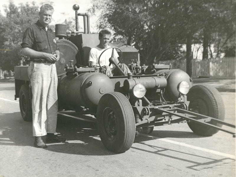 An old car from the 1950's where Safety Striping Service got there beginning with two men standing next to the car.